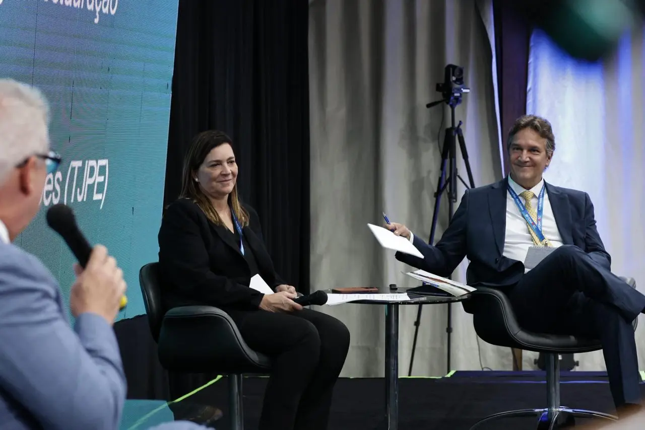 Foto que mostra o palco do auditório com o presidente do Fonamec, Erik Dantas falando ao microfone, de costas na foto. De frente para ele, sentados em poltronas, estão os conselheiros do CNJ, Mônica Autran e Alexandre Teixeira. 
