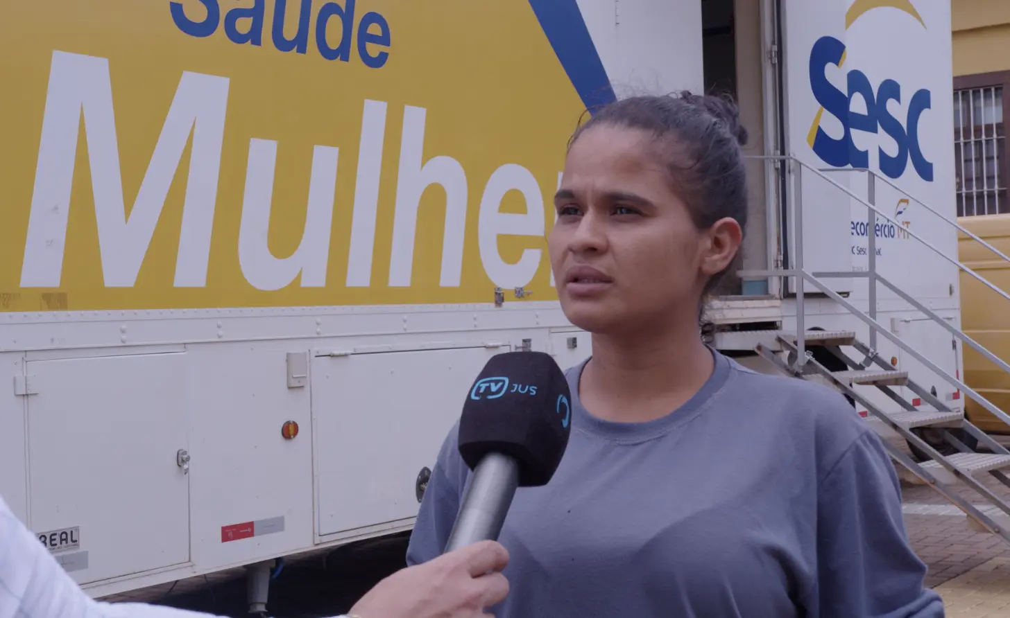 Maria José Oliveira durante entrevista à TV.Jus, em frente à carreta Sesc Saúde Mulher. ela é uma jovem de pele parda, cabelos castanhos presos, usando camiseta cinza.
