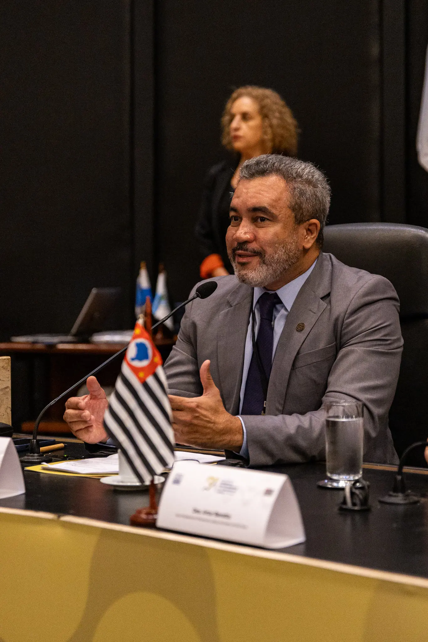 Juiz Antônio Peleja fala ao microfone. Ele está sentado e gesticula. Ele é um homem negro, de barba e cabelos grisalhos, usando camisa azul clara, gravata azul marinho e terno cinza.