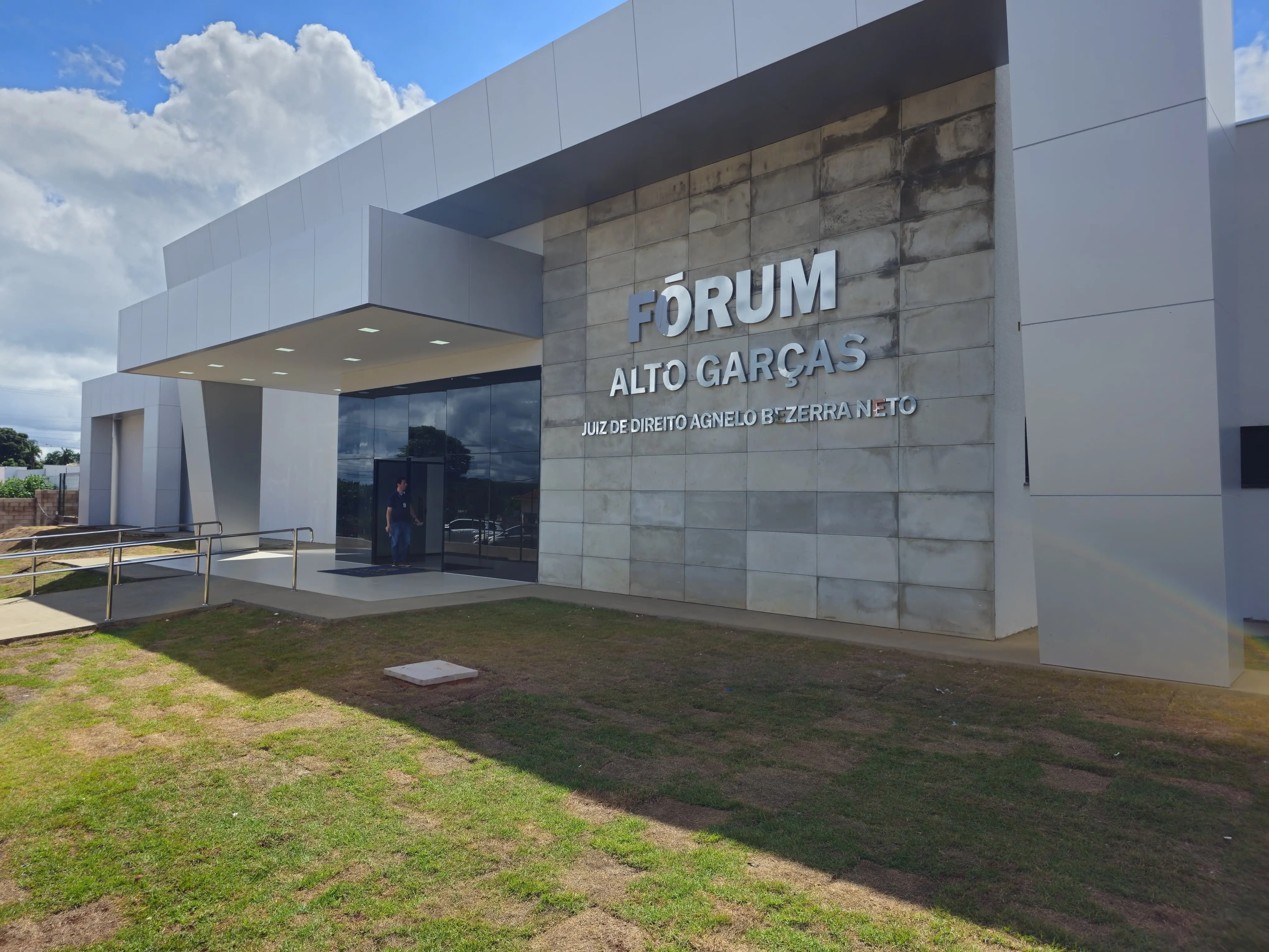 Foto horizontal colorida da fachada do Fórum de Alto Garças. A estrtrutura é na cor cinza, com pedras recortadas em destauqe. O nome do fórum está em letras garrafais prateadas