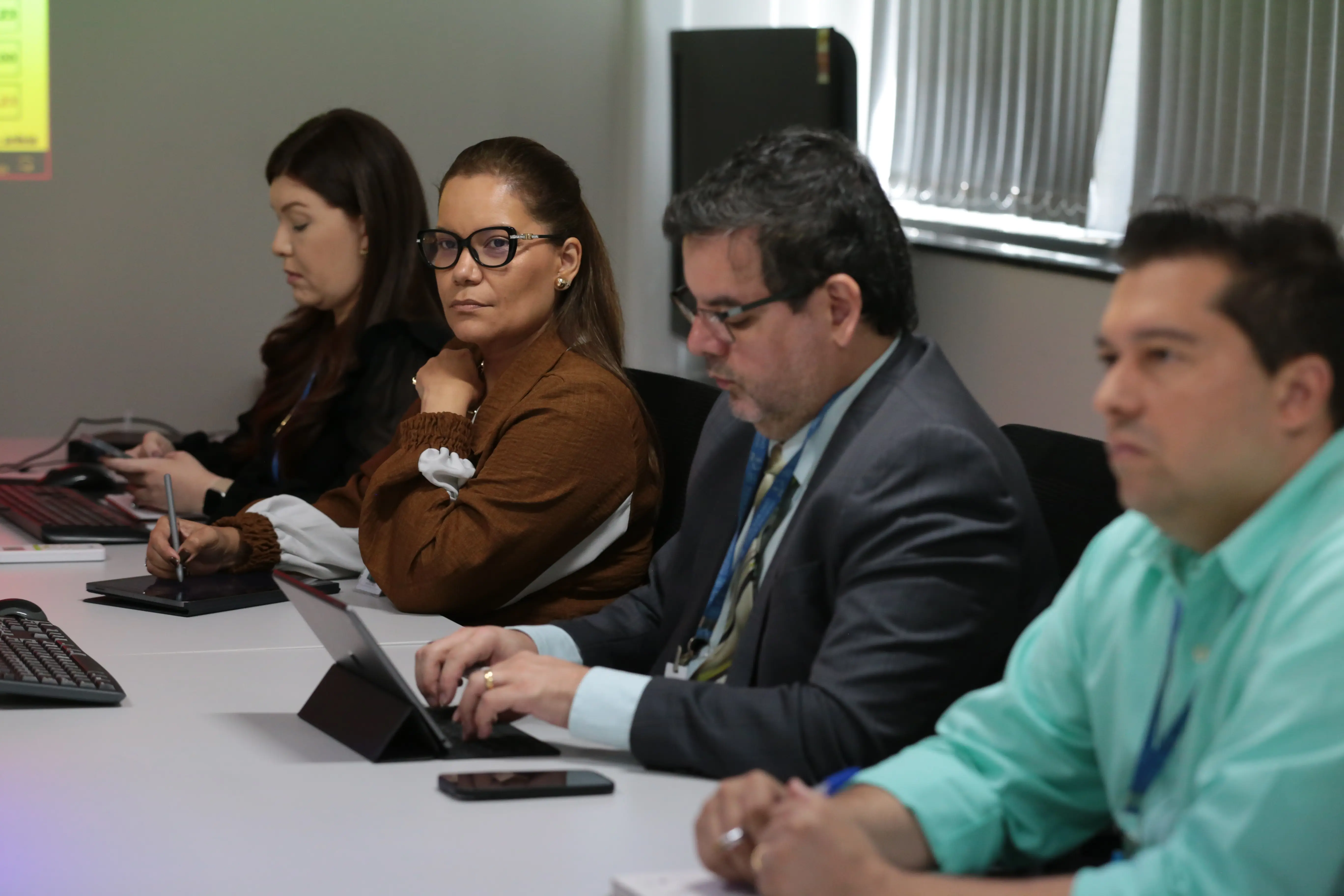 Foto que mostra duas mulheres e dois homens sentados em volta de uma mesa, na sala de reuniões. A segunda mulher é a coordenadora de Tecnologia da Informação do TJMT, Márcia Regina de Carvalho. Ela é uma mulher negra, de cabelo longo, liso e castanho, usando blusa de manga comprida marrom e branca. 