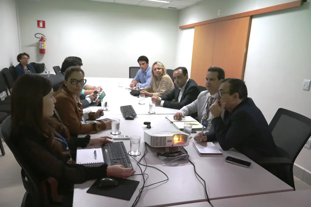 Foto que mostra várias pessoas sentadas em volta de uma mesa, participando de uma reunião.