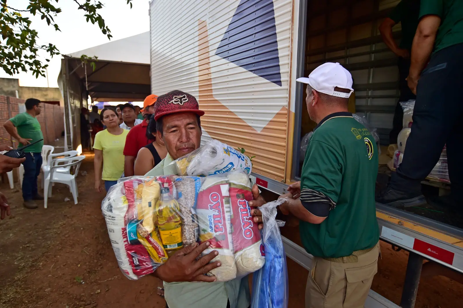 Homem recebe doação de cesta básica das mãos de voluntário da Expedição Justiça Sem Fronteiras, em frente ao caminhão da Defesa Civil.