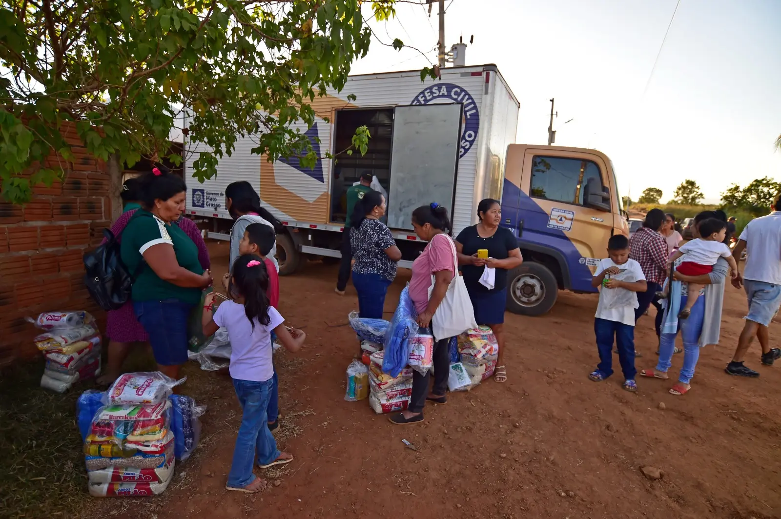 Várias pessoas recebem doações de cestas básicas em frente ao caminhão da Defesa Civil.