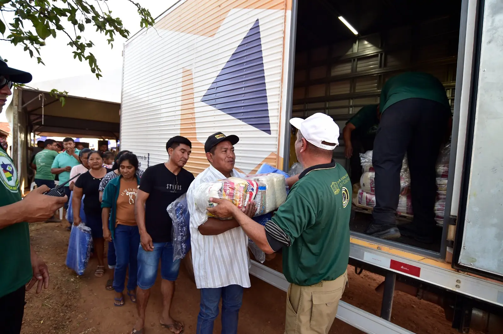 Pessoas em fila recebe doação de cestas básicas em frente ao caminhão da Defesa Civil.