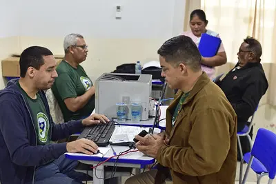 Em uma sala de aula, servidores do INSS atendem cidadãos.