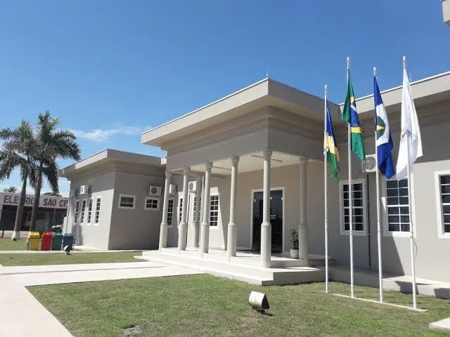 Fachada do Fórum de Guarantã do Norte tirada de lado. O prédio tem estilo neoclássico, com colunas, palmeiras e mastros com bandeiras no gramado.