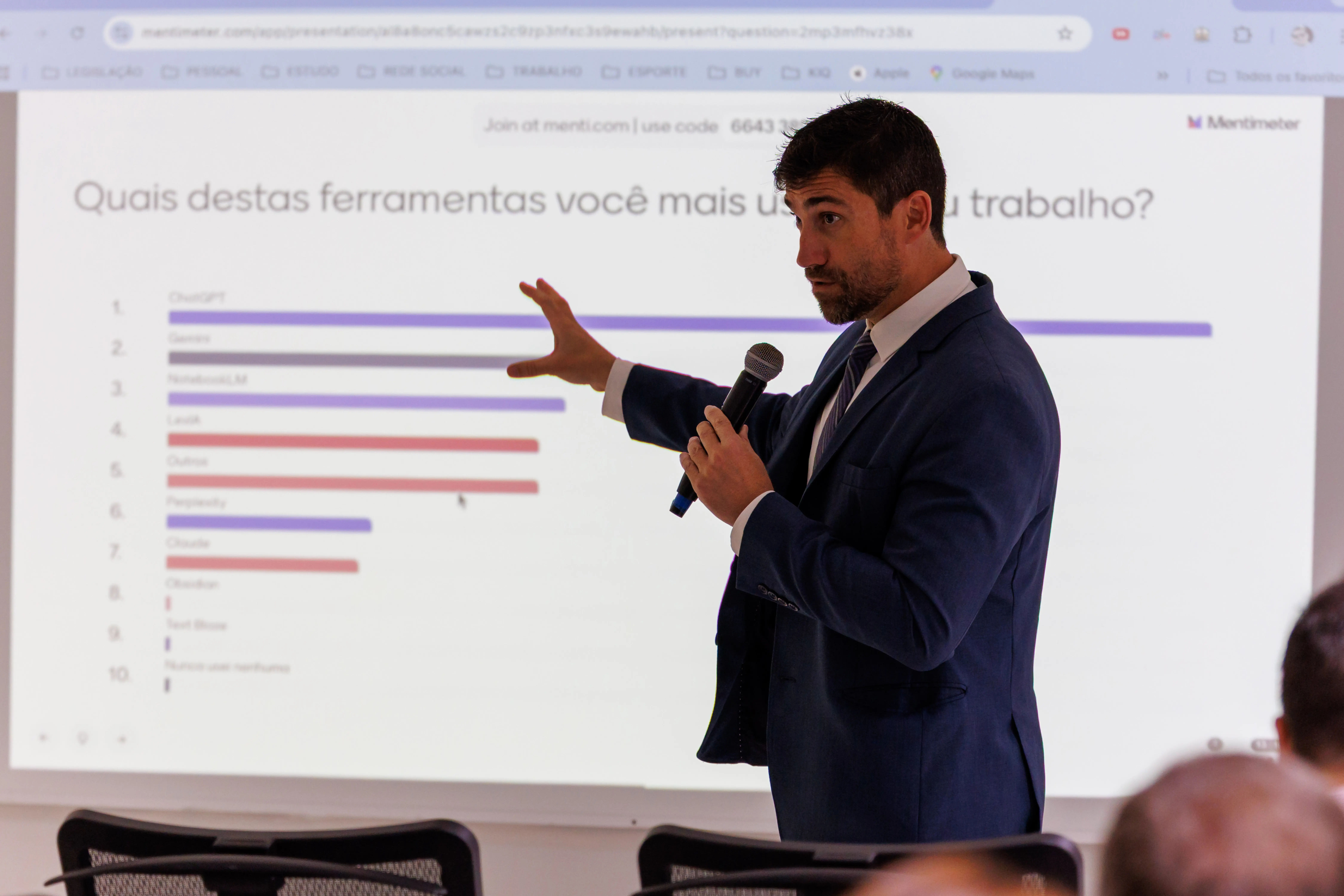 Desembargador Lídio Modesto. Homem branco, com terno preto, camisa branca, em sala com luz clara, segurando microfone durante abertura de capacitação sobre inteligência artificial.
