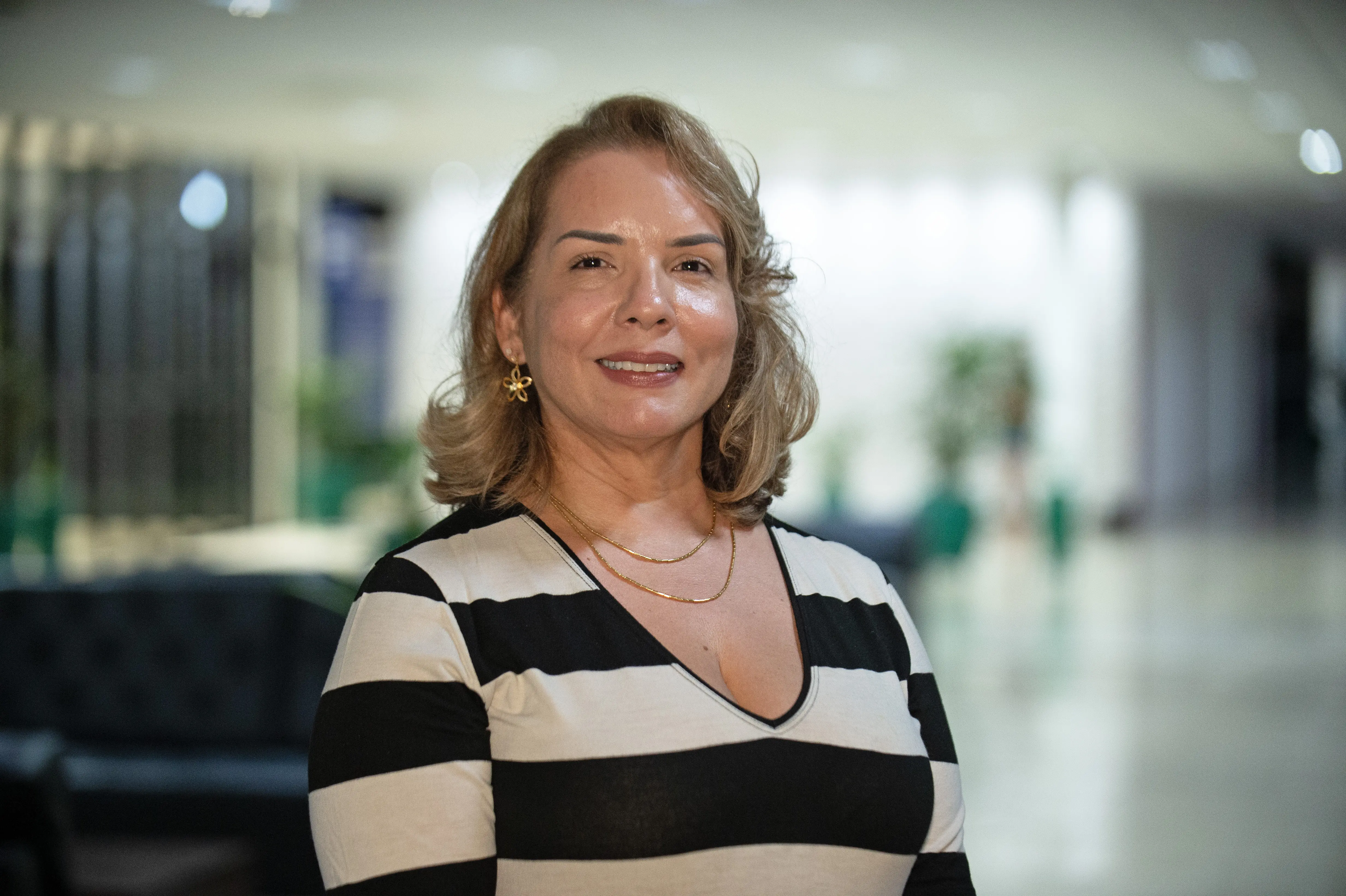 servidora Phiama posa para foto. Ela está como gestora geral do fórum de Cuiabá. É uma mulher branca, de cabelos curtos e loiros. Usa uma blusa de manga comprida litrada de preto e branc o