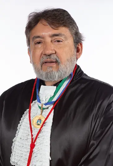 Des. Márcio Vidal posa para retrato oficial. Ele veste toga preta da magistratura, tem cabelos grisalhos e barba bem aparada. No peito, destaca-se uma medalha dourada pendurada por uma fita com as cores azul, branco e verde, simbolizando uma condecoração de mérito judiciário.