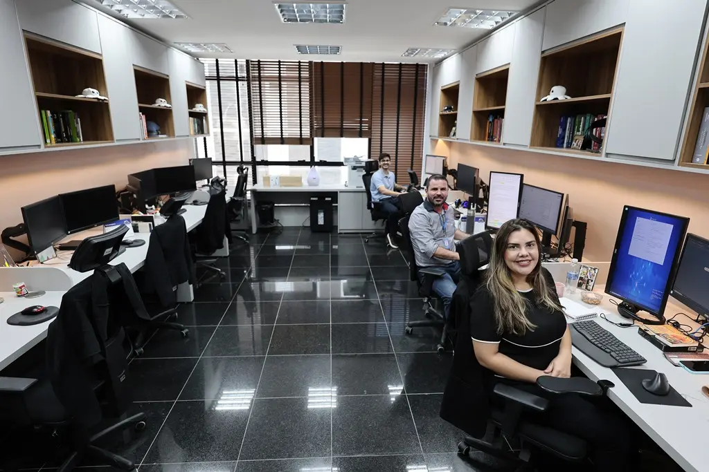 foto horizontal de uma sala onde há dois homens e uma mulher sentados em frente a computadores, virados para a foto e sorrindo. A sala é da assessoria de algum desembargador do Tribunal de Justiça.