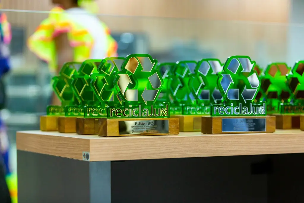 Foto colorida, na horizontal, que mostra uma mesa com vários troféus do Reciclajud. Os troféus são verdes e têm o símbolo da reciclagem e a palavra ReciclaJud.
