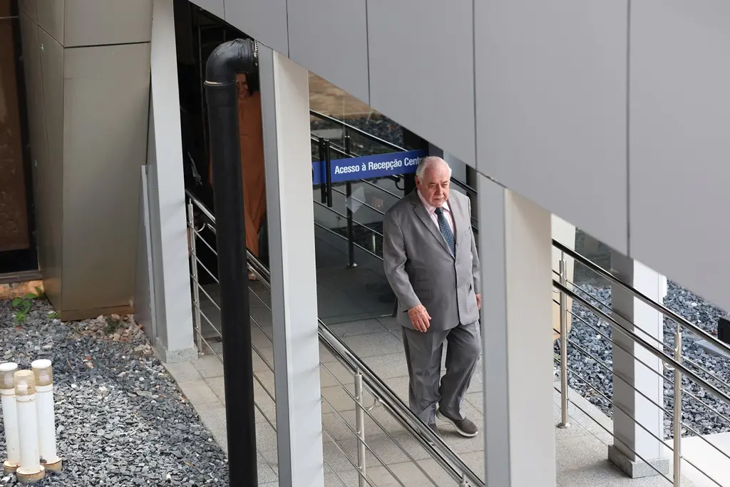 Foto horizontal que mostra o presidente do TJMT, desembargador José Zuquim Nogueira, subindo a rampa que dá acesso ao Plenário 1 do Tribunal. Ele é um senhor branco, de cabelos brancos, de estatuto baixa e obeso. Ele usa terno e calça social cinzas.