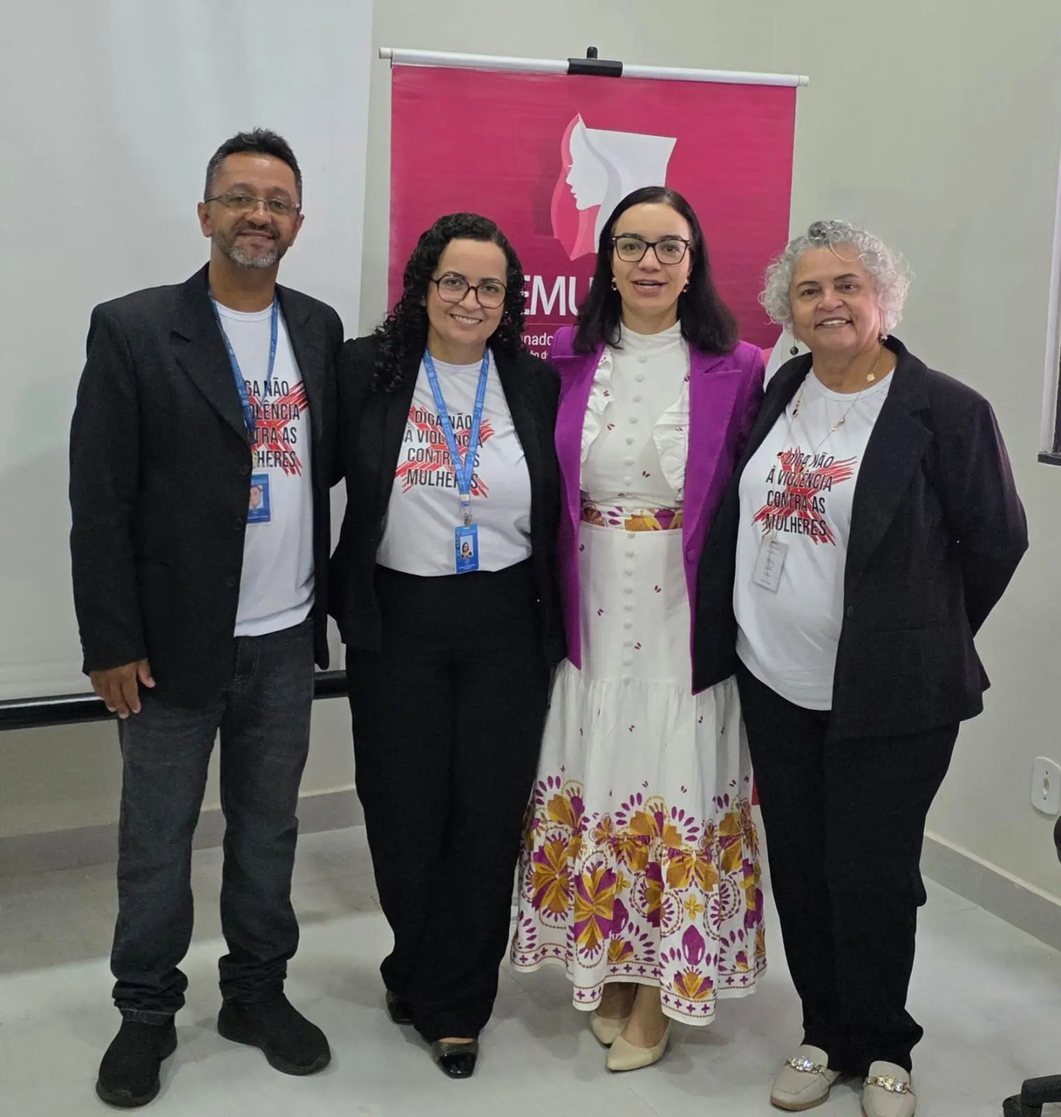 Foto de quatro integrantes da equipe CEMULHER-MT, vestindo blazers e camisetas personalizadas, posando sorrindo. 