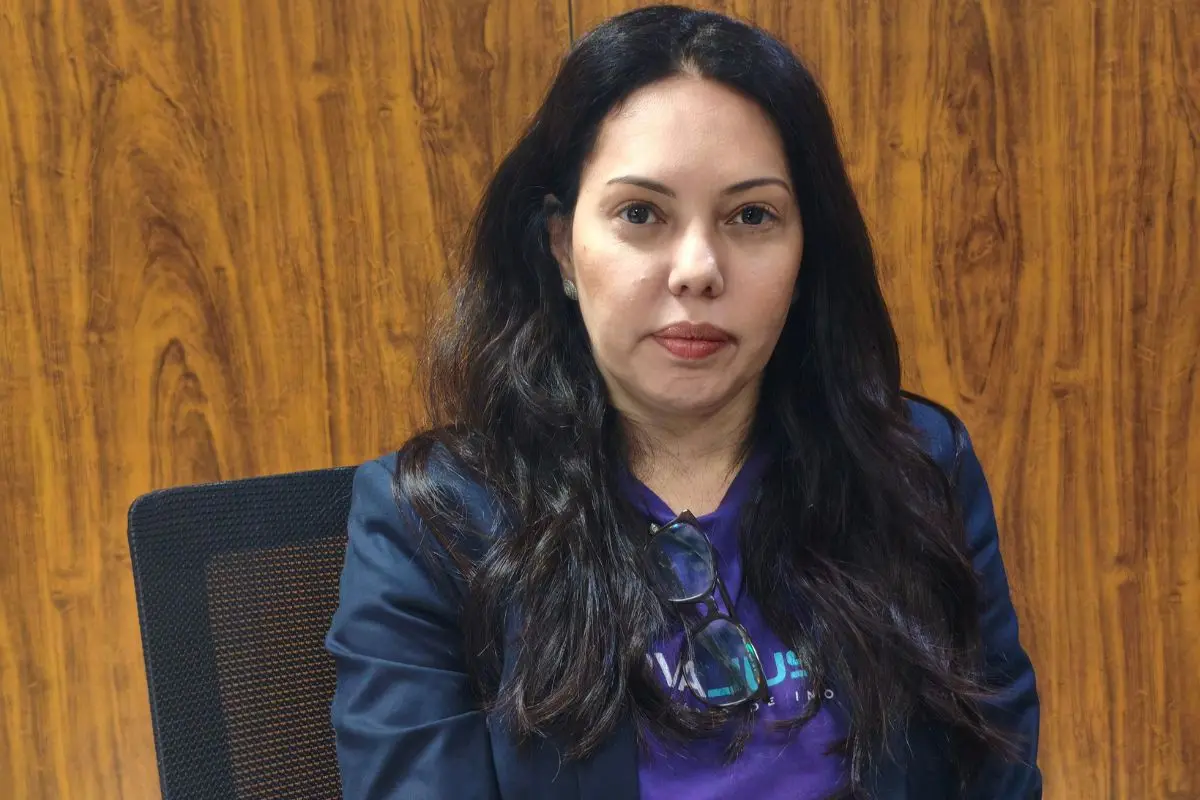 Foto em plano fechado que mostra a juíza Joseane Quinto, uma mulher branca, de cabelos longos e escuros, vestindo blazer azul sobre camiseta roxa. Ela olha diretamente para a câmera.