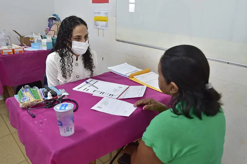 Foto que mostra uma mulher de costas, sendo atendida por uma médica da Prefeitura de Vila Bela da Santissima Trindade, em uma sala de aula, durante a Expedição Justiça Sem Fronteiras.
