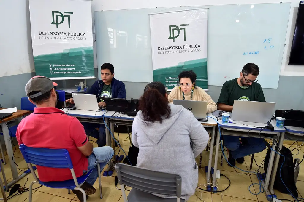 Foto que mostra servidores e defensor público estadual atendendo pessoas em uma sala de aula, no mutirão da Justiça Sem Fronteiras.