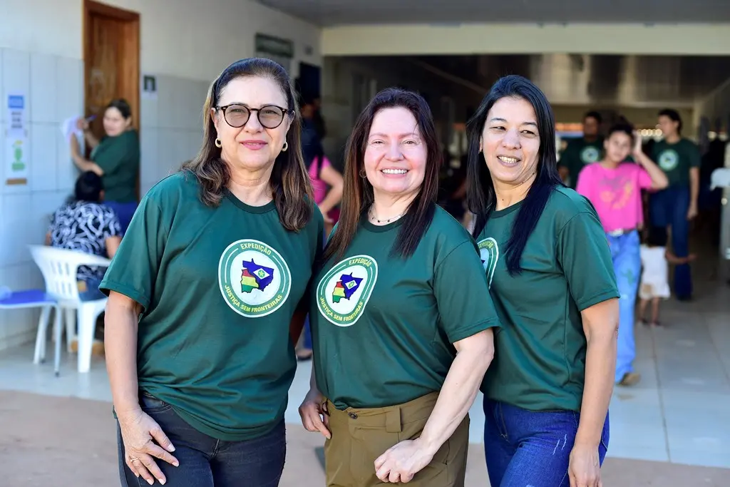Foto que mostra três mulheres usando a camiseta verde da Justiça Sem Fronteiras e sorrindo para a foto. 