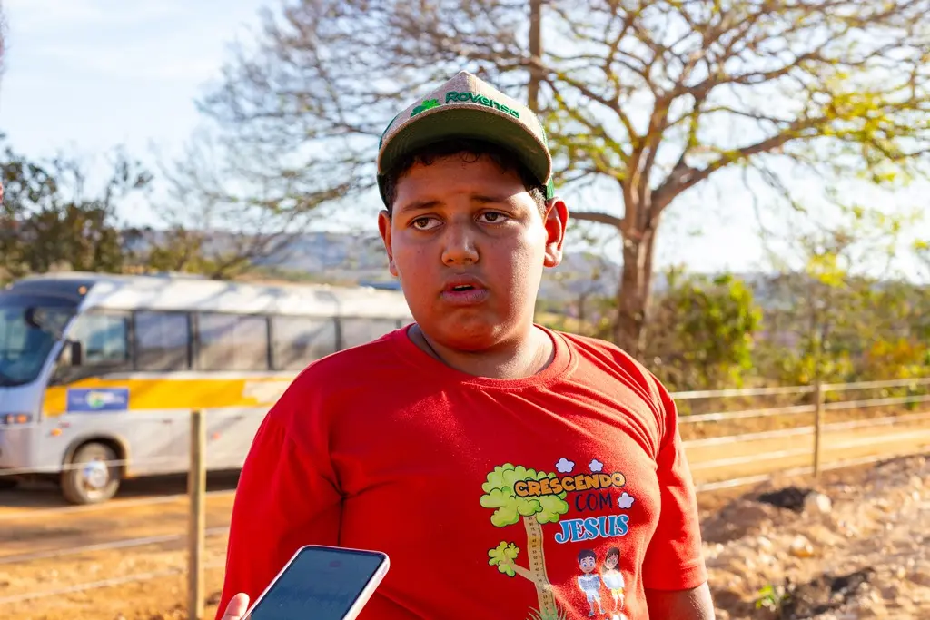 O menino Ruan Carlos, 11 anos, concede entrevista. no ambiente do plantio de mudas. Ele é negro, de olhos escuros, usando camiseta vermelha estampada e boné.