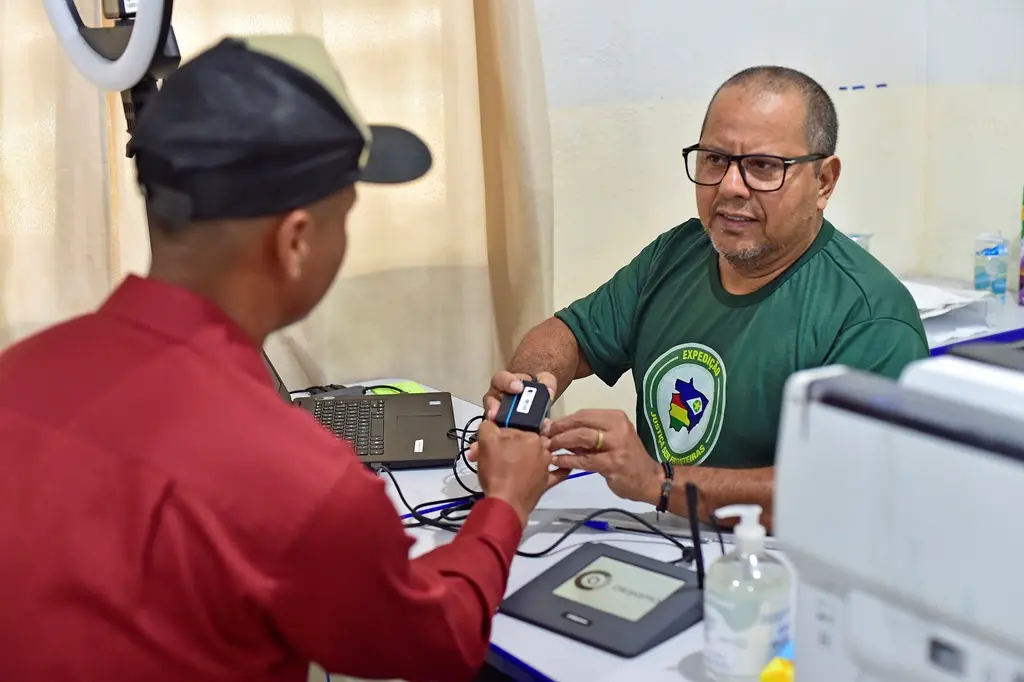 Foto que mostra um servidor da Justiça Eleitoral coletando a biometria de um cidadão, que aparece de costas na foto.