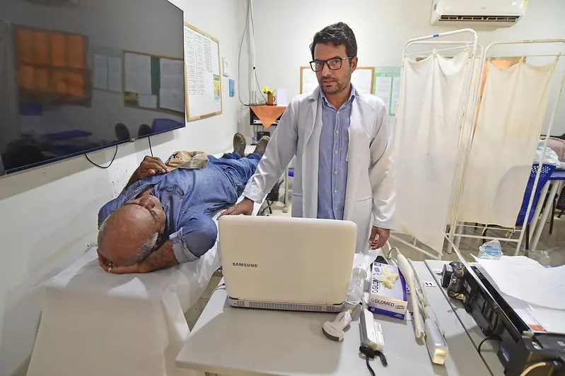 Foto que mostra um médico atendendo um paciente, que está deitado na maca, aguardando para fazer ultrassonografia.