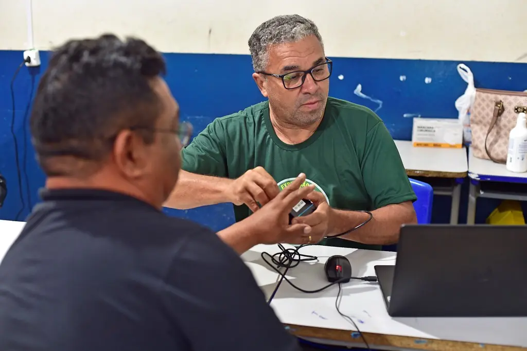 Servidor da Justiça Federal, usando camiseta verde da Justiça Sem Fronteiras, coleta biometria de um cidadão, que aparece de costas na foto.