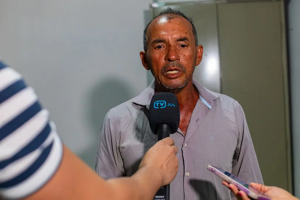 O eletricista Azinete Xavier Costa concede entrevista à TV.Jus. ele é um homem pardo, magro, cabelos e olhos castanhos, usando camisa social cinza.