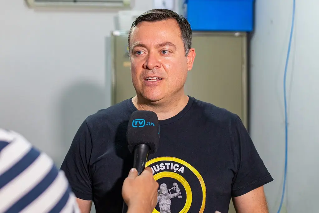 Juiz Leonísio Salles concede entrevista à TV Justiça. Ele é um homem branco, de olhos verdes, cabelo castanho claro, usando camiseta preta com logo da Justiça Comunitária.