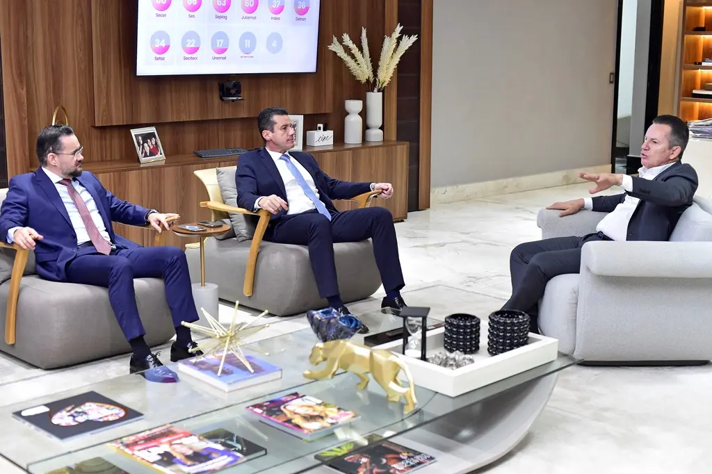 Em uma sala de reunião no Palácio do Governo, o governador Mauro Mendes, o desembargador Rodrigo Curvo e o juiz Bruno D'Oliveira estão sentados em poltronas, conversando.