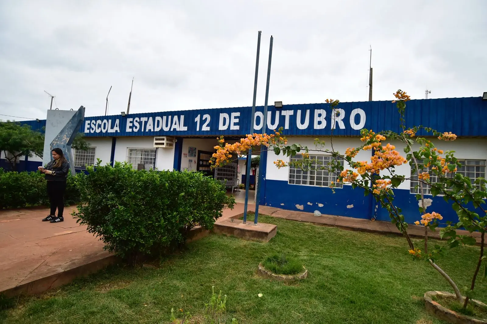 Fachada da Escola Estadual 12 de Outubro. A escola é azul e branca e tem um jardim em frente.