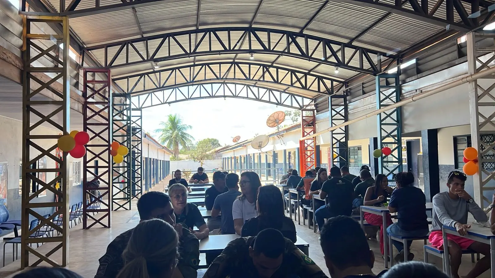 Foto do refeitório das Escolas 11 de Agosto e Ponta do Aterro repleta de pessoas comendo, sentadas. ao fundo, é possível ver o corredor das salas de aula.