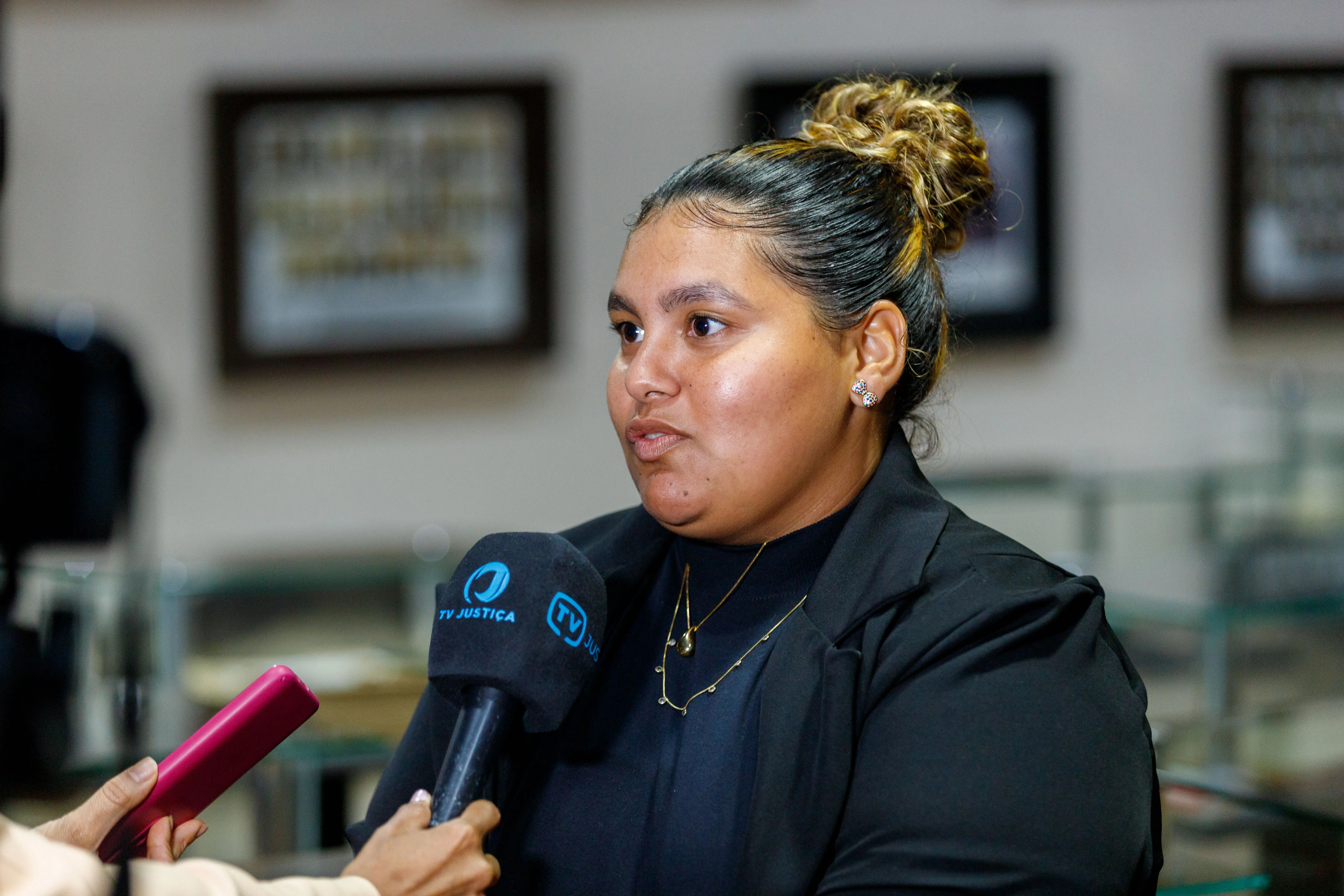 Aluna da Unic de Rondonópolis durante programa Nosso Judiciário. Ela é negra, cabelos pretos presos, usa blaser e blusa pretos