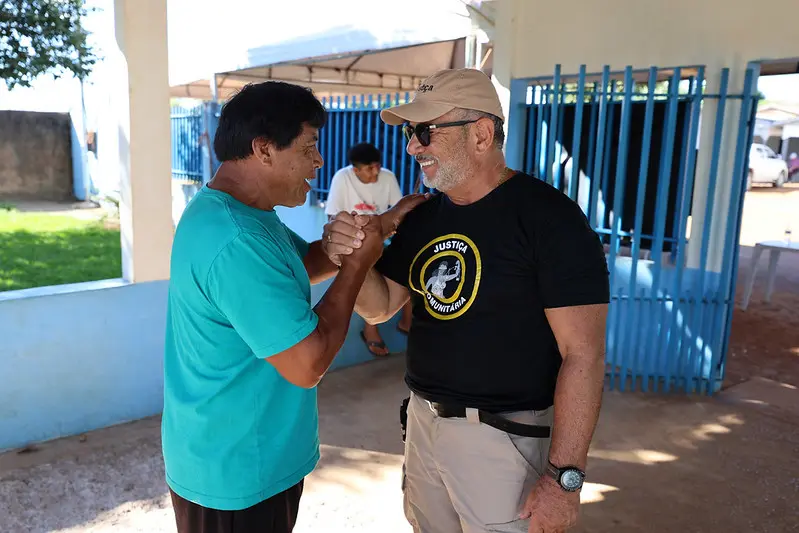 Foto horizontal colorida, em plano médio, que mostra o professor indígena Tirawa Waura e o juiz coordenador da Justiça Comunitária, José Antonio Bezerra Filho, se cumprimentando na entrada da escola onde ocorreu mutirão da Justiça em Ação. 