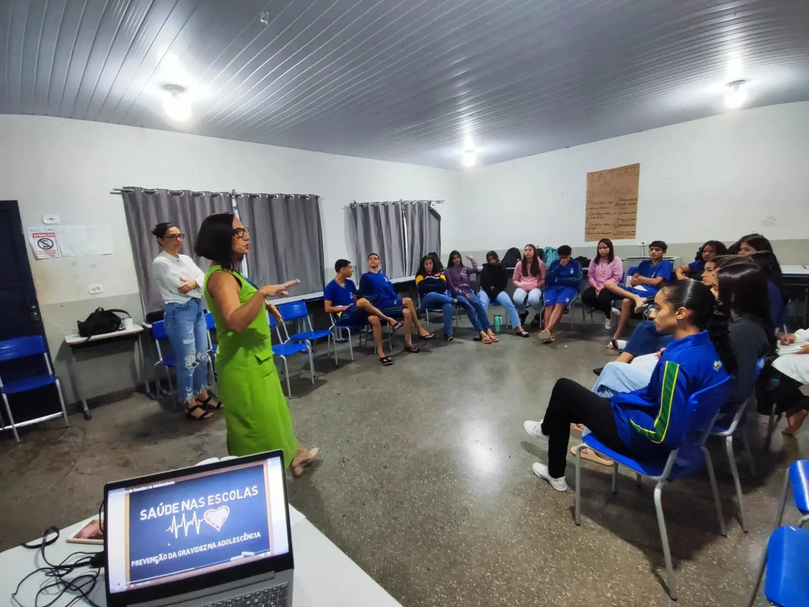 A agente da infância de São José dos Quatro Marcos faz palestra dentro de uma sala de aula, onde os jovens estão sentados em cadeiras, formando um semicírculo