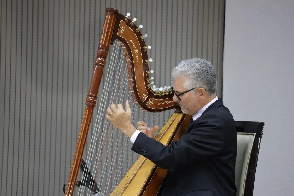Foto horizontal que mostra o harpista Narcizo Lucena tocando harpa no plenário do Tribunal de Justiça.