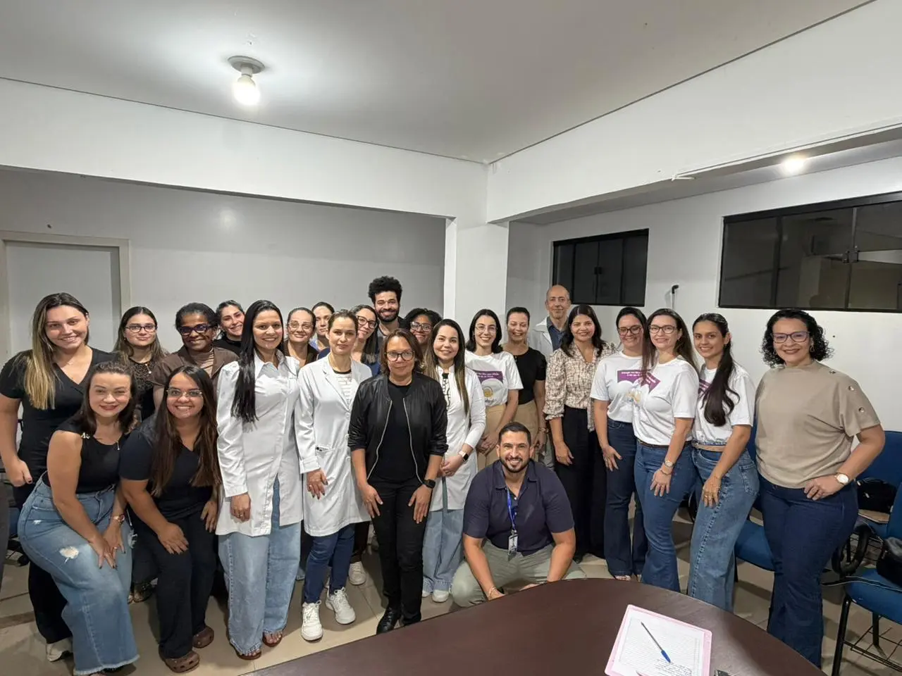 A juíza da 2ª Vara Cível de Tangará da Serra, Raiza Vitória de Castro Rego Bastos Gonzaga, a equipe da Vara da Infância e Juventude e profissionais do Hospital Municipal Arlete Daisy Cichetti de Brito estão em uma sala de reuniões do hospital municipal, perfilados, em pé e sentados.