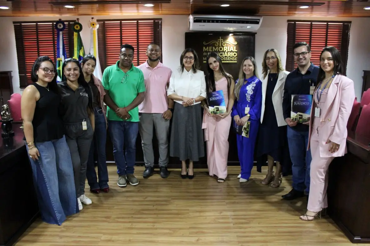 Foto horizontal que mostra um grupo de pessoas do Judiciário e estudantes de Direito da Fasipe Cuiabá posando para a foto, sorrindo, no Espaço Memória do Tribunal de Justiça.
