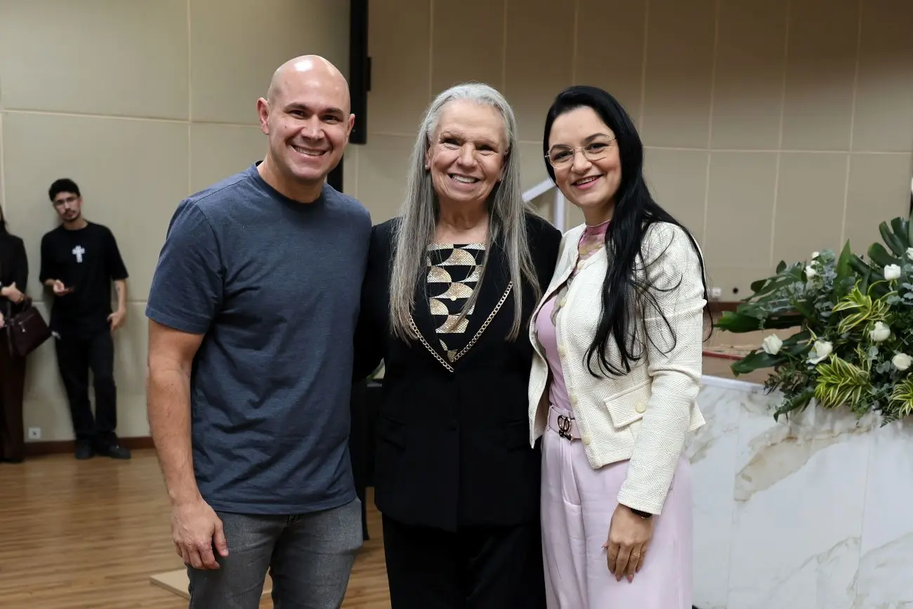 Foto horizontal que mostra a desembargadora Maria Erotides ladeada pelo prefeito Abilio Brunini e pela vereadora e primeira-dama Samantha Íris, no auditório do TJMT. eles estão sorrindo para a foto.