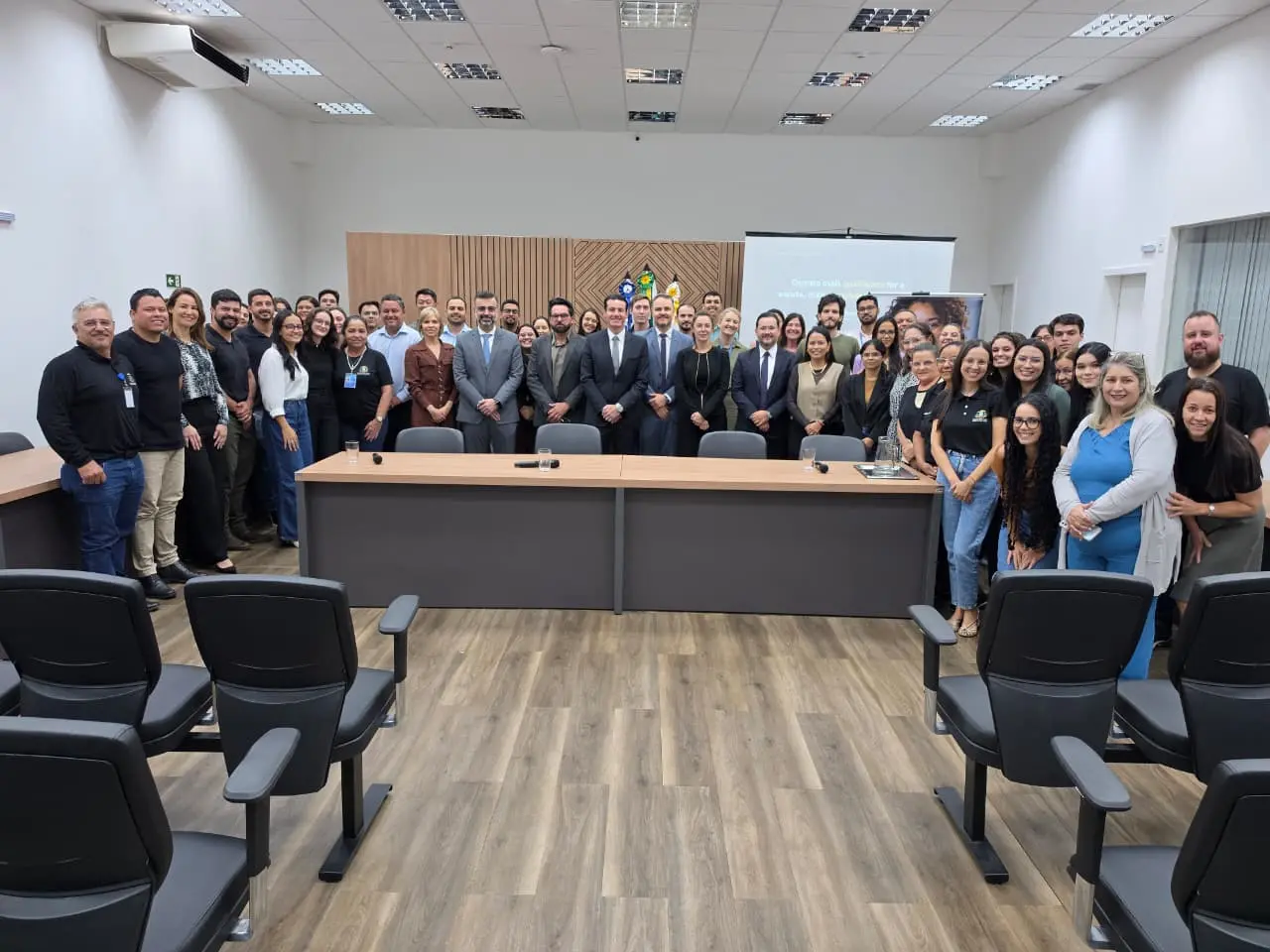 Foto horizontal em plano aberto que mostra cerca de 50 pessoas posando para a foto, no plenário do júri do Fórum de Tangará da Serra. Ao centro está o desembargador Rodrigo Curvo e magistrados. As outras pessoas são servidores da comarca.