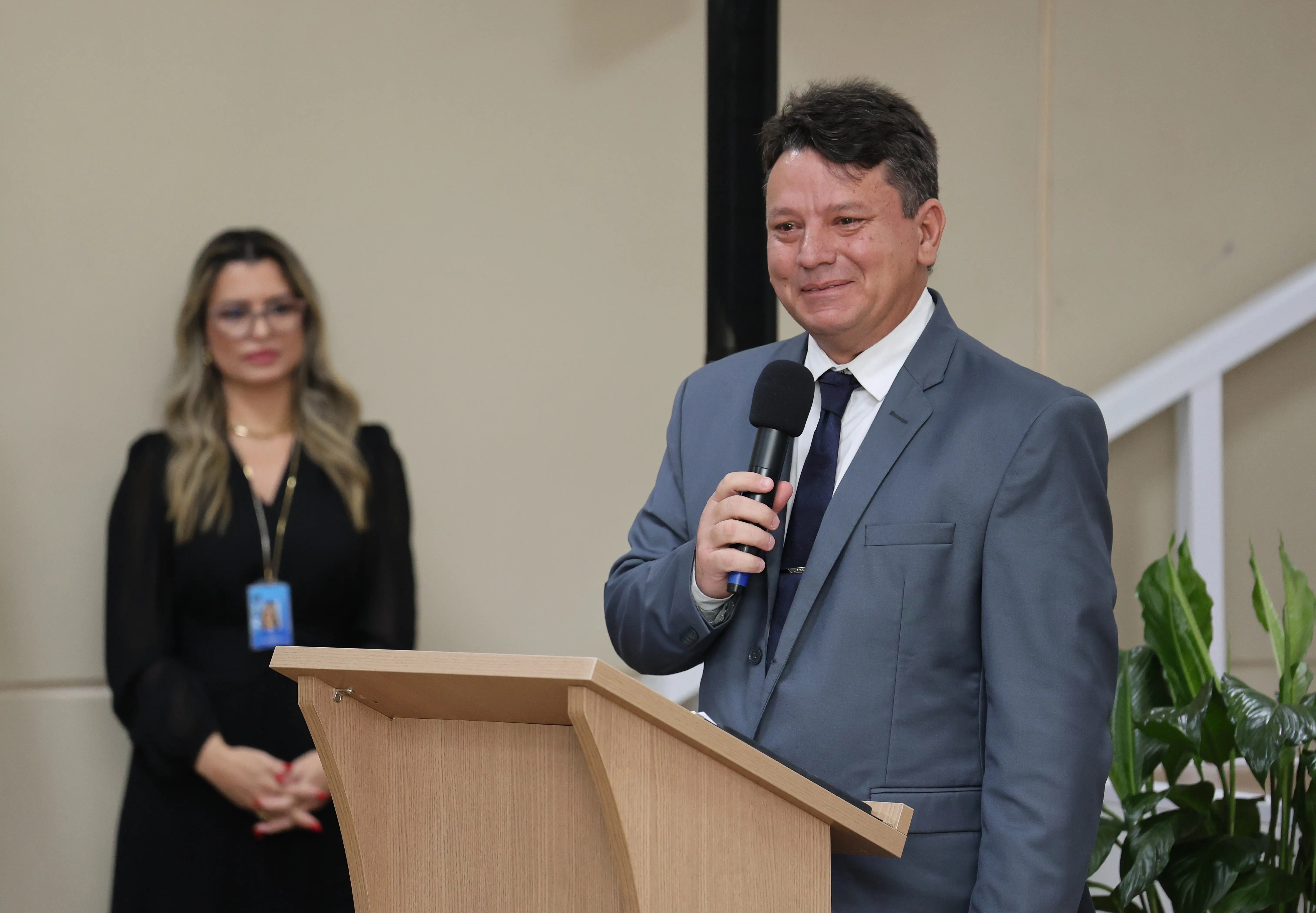 Foto horizontal que mostra Lucilo Macedo, filho da desembargadora Maria Erotides, falando ao microfone, no púlpito, com semblante emocionado. Ele é um homem branco, alto, de cabelo castanho, usando camisa branca, gravata preta e terno cinza.