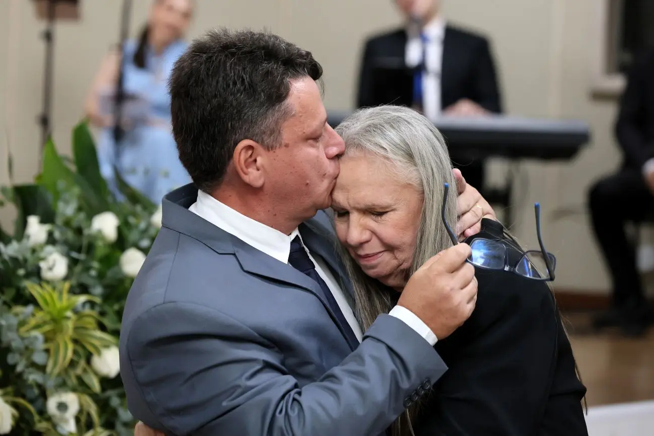 Foto horizontal que mostra o filho da desembargadora Maria Erotides a abraçando e beijando sua testa, no auditório do TJMT. 