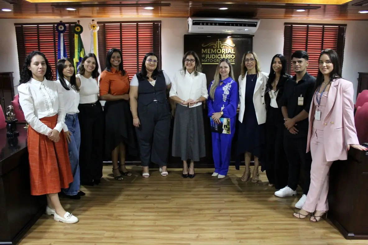 Foto horizontal que mostra um grupo de pessoas do Judiciário e estudantes de Direito da Fasipe Cuiabá posando para a foto, sorrindo, no Espaço Memória do Tribunal de Justiça.