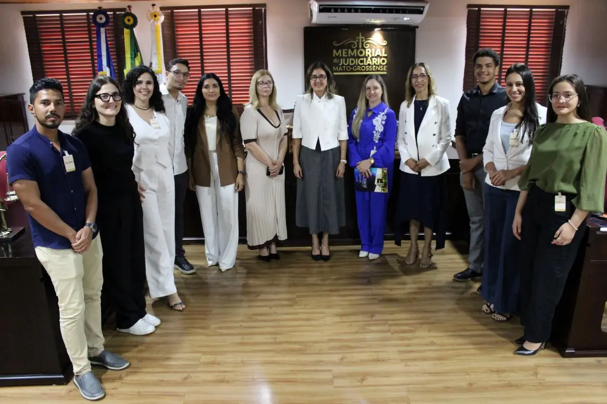 Foto horizontal que mostra um grupo de pessoas do Judiciário e estudantes de Direito da Fasipe Cuiabá posando para a foto, sorrindo, no Espaço Memória do Tribunal de Justiça.