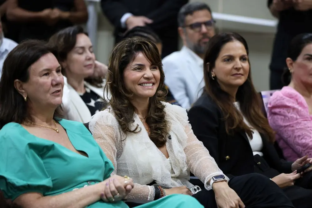 Foto horizontal que mostra, em primeiro plano, a desembargadora Helena Maria Bezerra Ramos, a defensora-pública geral Luziane Castro e a presidente da OAB Mato Grosso, Gisela Cardoso, sentadas na primeira fila do auditório do TJ. Luziane sorri.