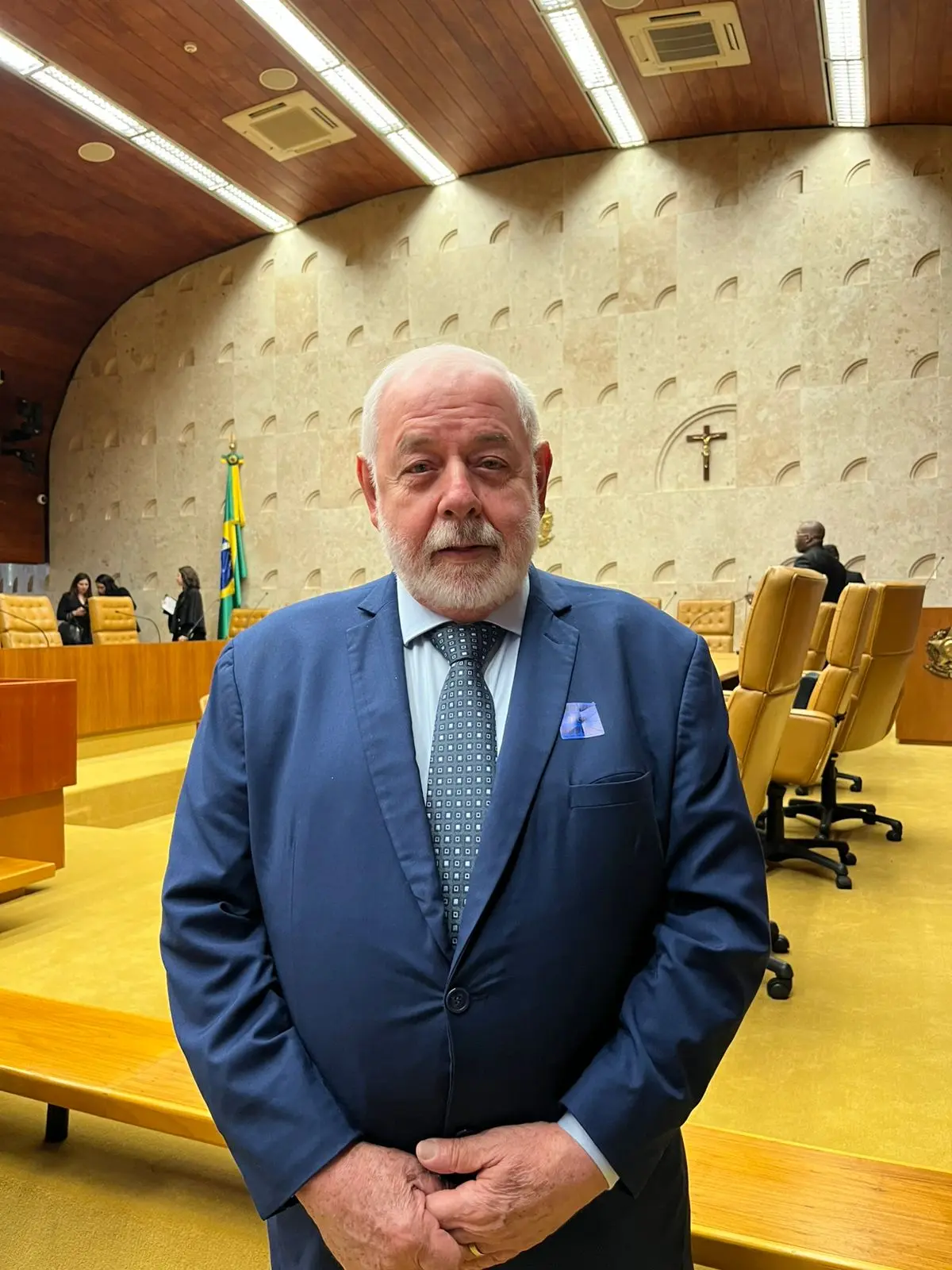 Foto colorida do presidente do TJMT, desembargador José Zuquim Nogueira, posando para a foto no Plenário do Supremo Tribunal Federal. Ele é um senhor branco, de cabelos e barba grisalhos, olhos claros, usando camisa e gravata cinza e terno azul.