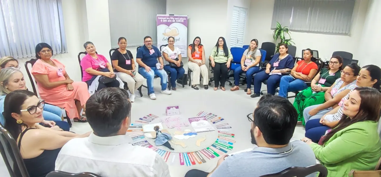 Pessoas sentadas em círculo no que parece ser uma reunião ou treinamento. Há um diagrama circular no chão no centro do grupo e um banner com o logo "Entrega Legal".