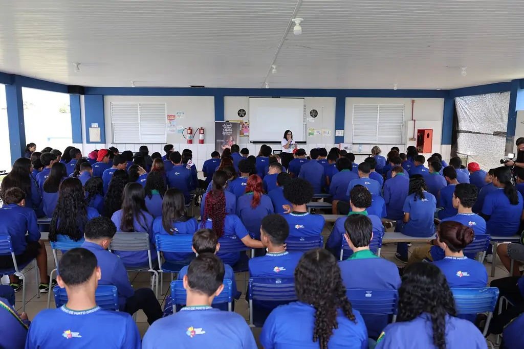 Foto horizontal em plano aberto que mostra o pátio da escola repleto de alunos sentados, assistindo a palestra da Cemulher.