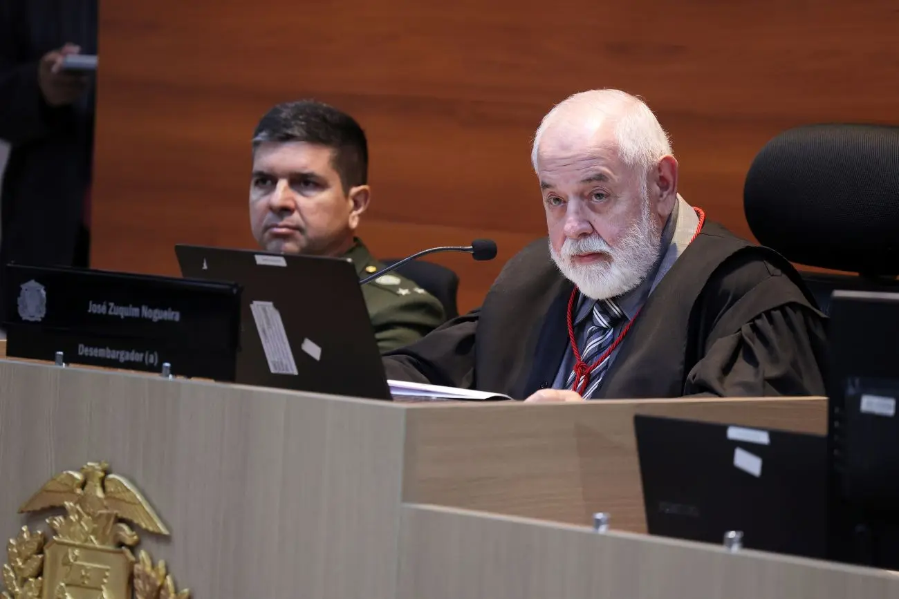 Foto horizontal que mostra o presidente do TJMT, desembargador José Zuquim Nogueira, sentado no plenário do Tribunal, usando toga. Um comandante do Exército está sentado ao lado dele.