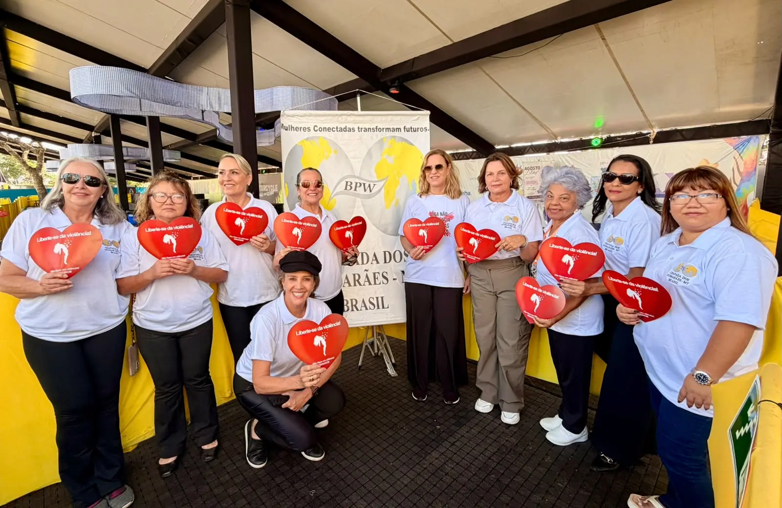 Foto que mostra a equipe da Cemulher e da BPW posando para foto. Todas seguram um panfleto em formato de coração referente ao fim da violência doméstica.