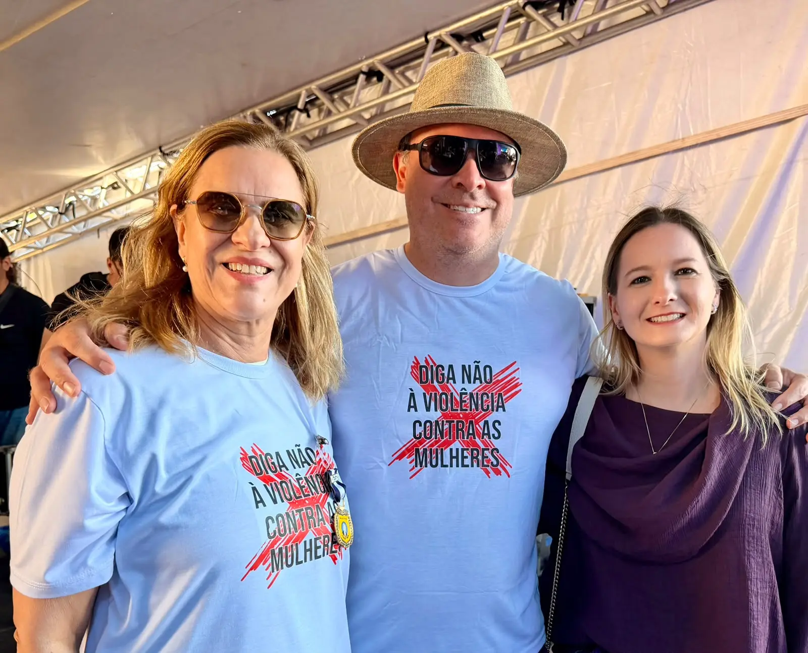 Foto que mostra a desembargadora Vandymara Galvão, o juiz Leonísio Salles e a juíza Djessica Kuntzer sorrindo para a foto. Os dois primeiros usam camiseta branca com a estampa que diz "Diga não à violência contra as mulheres". 